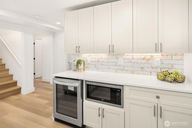 kitchen featuring light countertops, wine cooler, white cabinetry, stainless steel microwave, and backsplash