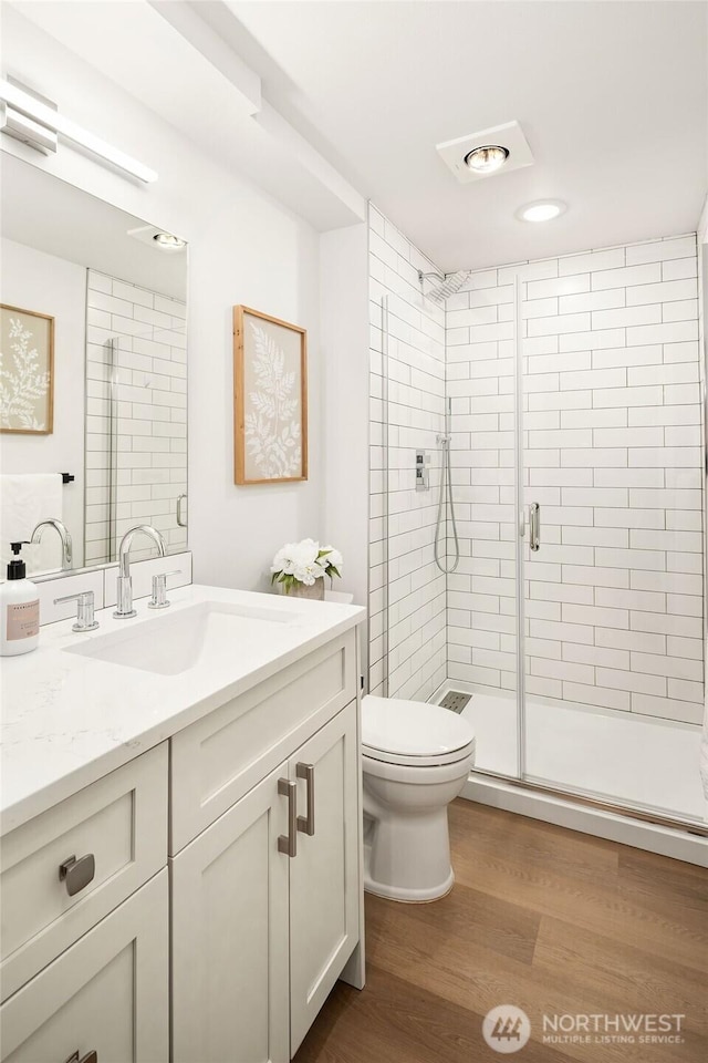 bathroom with wood finished floors, toilet, a stall shower, and vanity