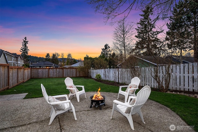 patio terrace at dusk featuring a lawn, an outdoor fire pit, and a fenced backyard