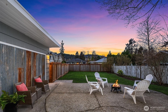 patio terrace at dusk with a lawn, an outdoor fire pit, and a fenced backyard