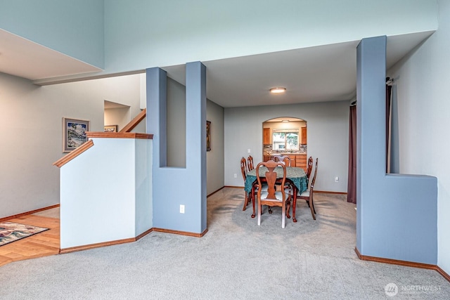 carpeted dining room featuring stairway, baseboards, and arched walkways