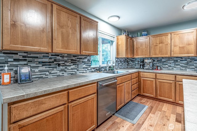 kitchen featuring light wood finished floors, dishwasher, light countertops, decorative backsplash, and a sink