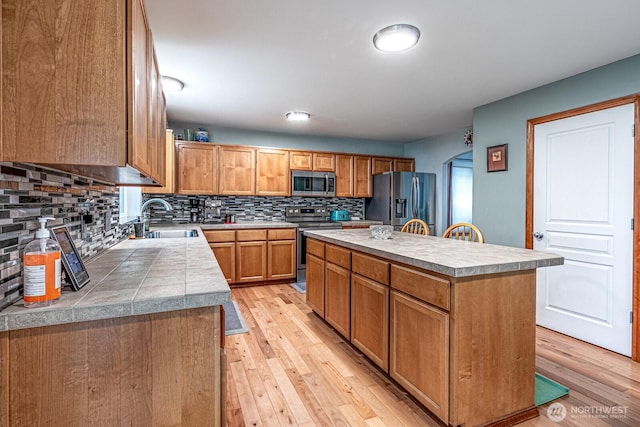 kitchen featuring arched walkways, stainless steel appliances, light wood-type flooring, and a sink