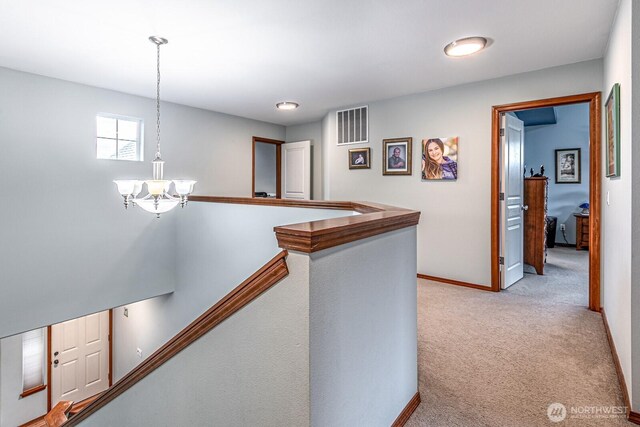 corridor with visible vents, light carpet, baseboards, and a chandelier