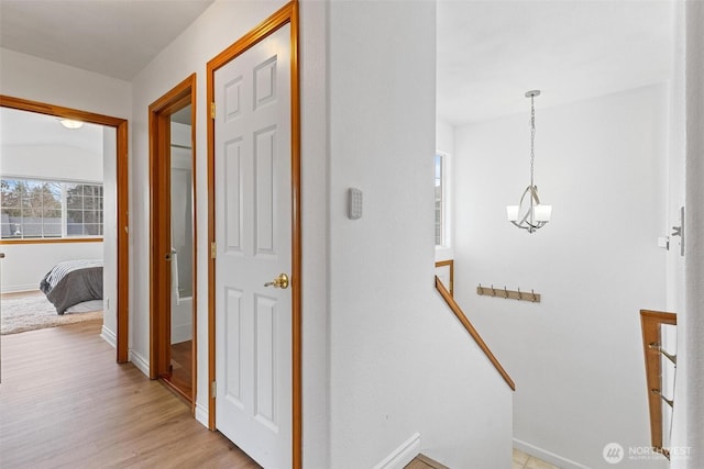 corridor with light wood-style flooring, an upstairs landing, and baseboards