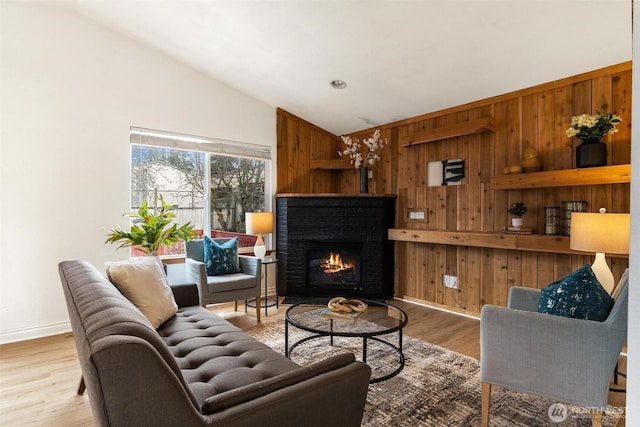 living room featuring wooden walls, baseboards, vaulted ceiling, a fireplace, and wood finished floors