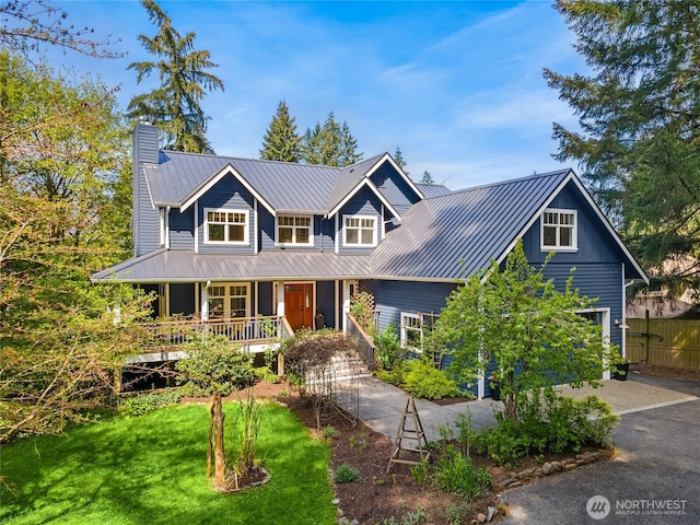 view of front of house with a front lawn, a chimney, a standing seam roof, covered porch, and metal roof