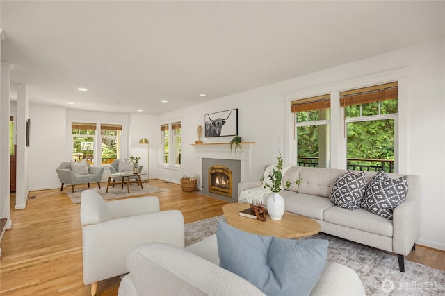 living area with light wood-style floors, baseboards, recessed lighting, and a fireplace with flush hearth