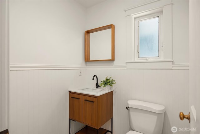half bathroom featuring vanity, wainscoting, and toilet