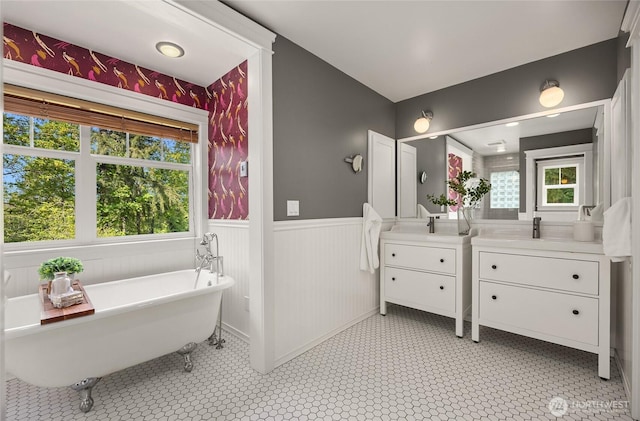 bathroom with a freestanding bath, tile patterned flooring, two vanities, a sink, and a wainscoted wall