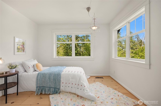 bedroom with visible vents, baseboards, wood finished floors, and a chandelier