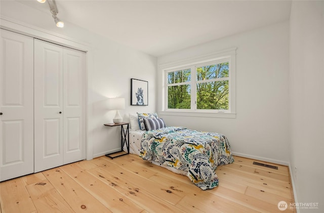 bedroom with track lighting, hardwood / wood-style floors, baseboards, visible vents, and a closet