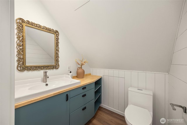 half bath with vanity, lofted ceiling, toilet, and wood finished floors