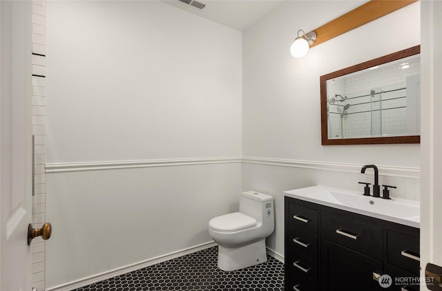full bath featuring vanity, toilet, tile patterned floors, a wainscoted wall, and a tile shower
