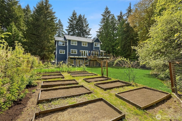 rear view of property featuring fence, stairway, a garden, a yard, and metal roof