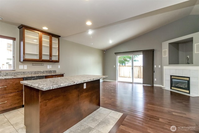 kitchen featuring light wood-style flooring, open floor plan, a center island, glass insert cabinets, and lofted ceiling