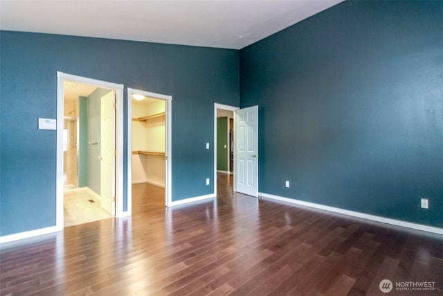 unfurnished bedroom featuring vaulted ceiling, a walk in closet, baseboards, and wood finished floors