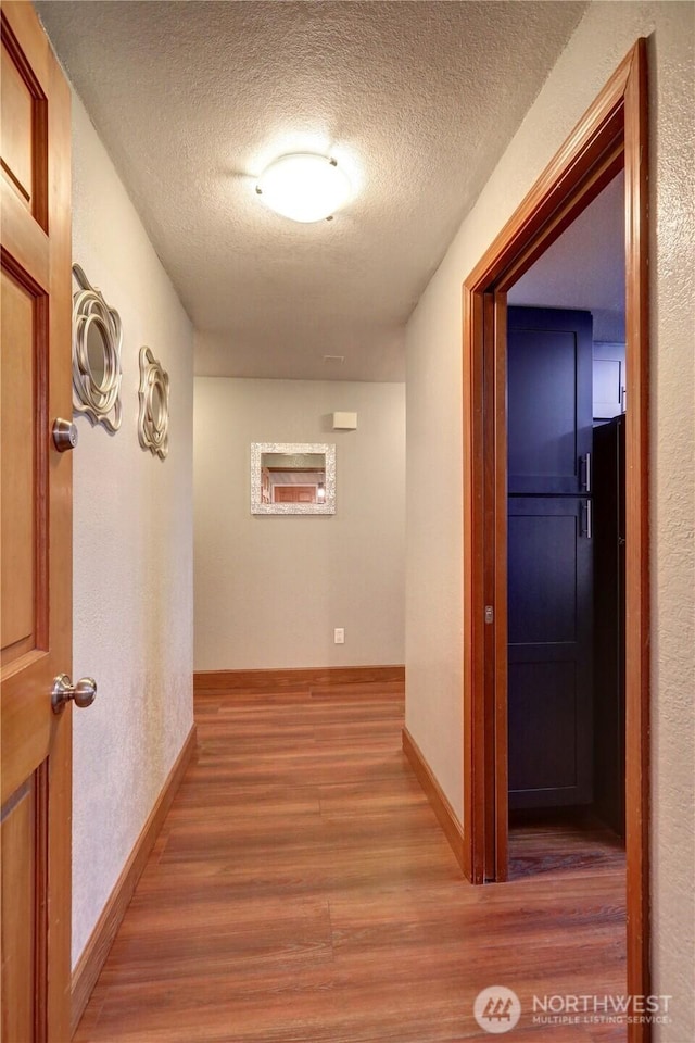 corridor with a textured ceiling, baseboards, and wood finished floors