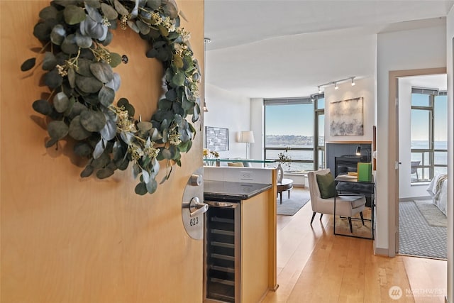 kitchen with a water view, beverage cooler, track lighting, dark countertops, and light wood finished floors