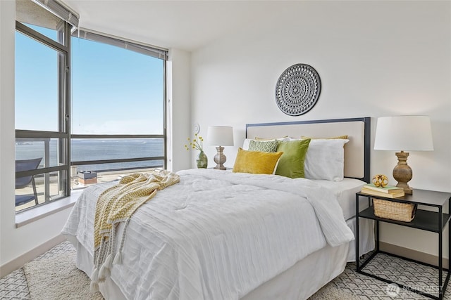 bedroom with floor to ceiling windows, baseboards, and a water view