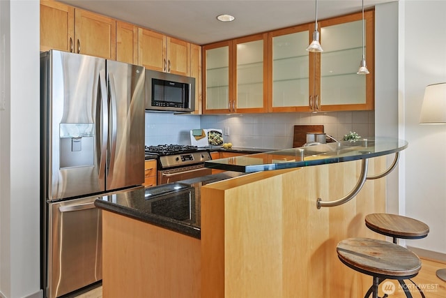 kitchen with a breakfast bar, tasteful backsplash, appliances with stainless steel finishes, a peninsula, and glass insert cabinets