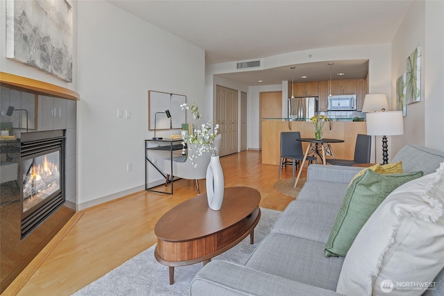 living room featuring visible vents, baseboards, light wood-style floors, and a tiled fireplace