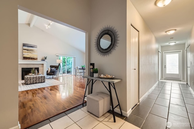 hallway featuring beam ceiling, tile patterned floors, high vaulted ceiling, and baseboards