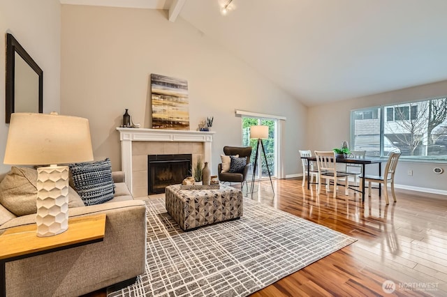 living area with baseboards, a tiled fireplace, beam ceiling, wood finished floors, and high vaulted ceiling