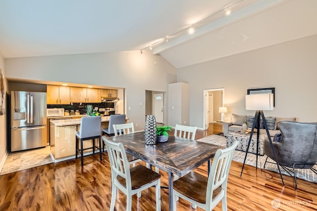 dining room with track lighting, wood finished floors, and high vaulted ceiling