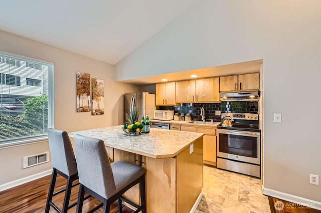 kitchen with visible vents, light brown cabinetry, a sink, a kitchen island, and appliances with stainless steel finishes