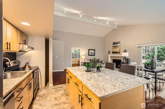 kitchen with a tiled fireplace, lofted ceiling, light brown cabinetry, under cabinet range hood, and dishwasher