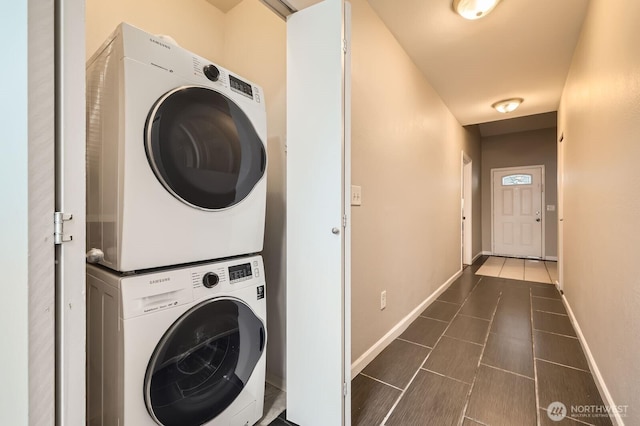 clothes washing area featuring dark tile patterned floors, laundry area, baseboards, and stacked washer and dryer