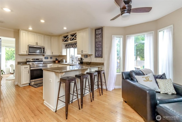 kitchen featuring a breakfast bar, a peninsula, a sink, light wood-style floors, and appliances with stainless steel finishes