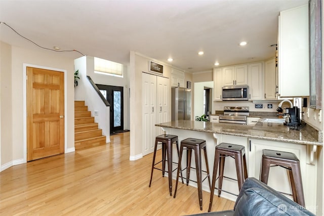 kitchen with light stone countertops, appliances with stainless steel finishes, a peninsula, light wood-style floors, and a sink