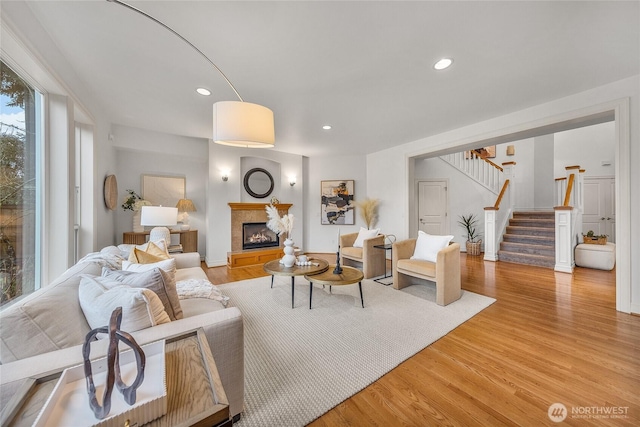 living room with a glass covered fireplace, stairs, recessed lighting, and light wood-type flooring