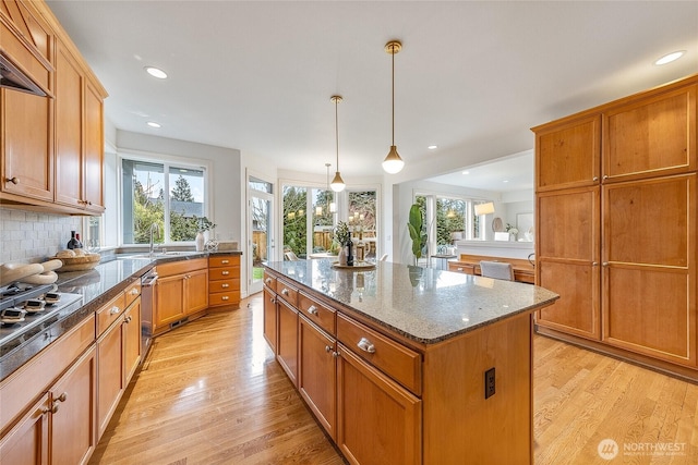 kitchen with backsplash, a center island, dark stone counters, light wood-style floors, and stainless steel gas stovetop