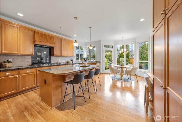 kitchen featuring light wood finished floors, tasteful backsplash, a center island, stainless steel gas cooktop, and a kitchen breakfast bar