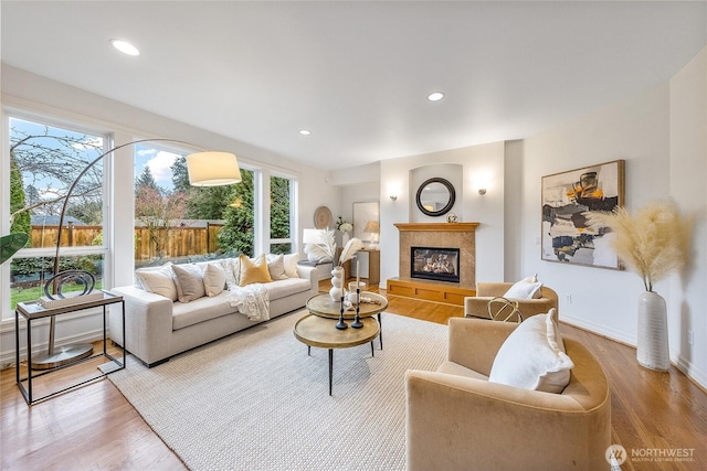 living room featuring a glass covered fireplace, recessed lighting, baseboards, and light wood-style floors