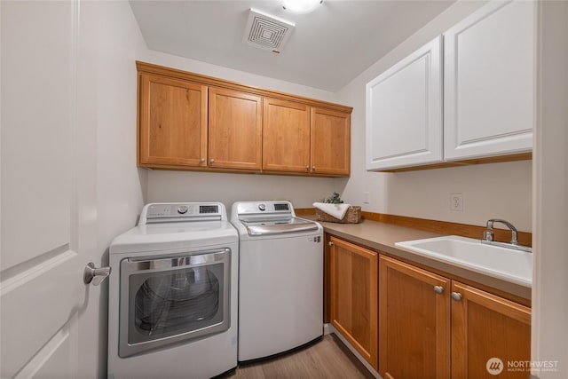 laundry area with visible vents, washer and clothes dryer, a sink, cabinet space, and light wood finished floors