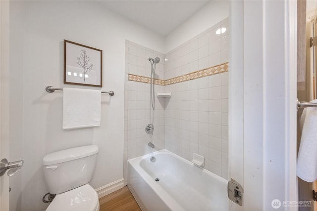 bathroom with wood finished floors, toilet, washtub / shower combination, and baseboards