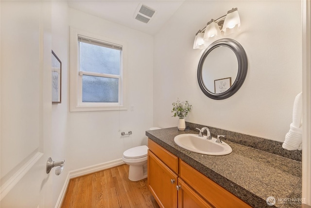 half bath with vanity, wood finished floors, visible vents, baseboards, and toilet