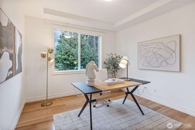 office space featuring baseboards, a raised ceiling, and wood finished floors