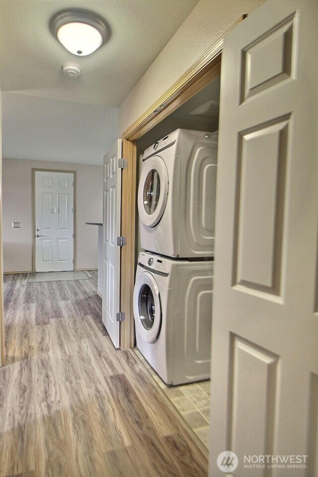 clothes washing area featuring stacked washer / dryer, laundry area, and wood finished floors