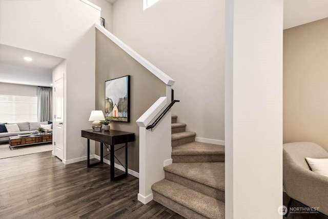 stairway with a high ceiling, recessed lighting, wood finished floors, and baseboards