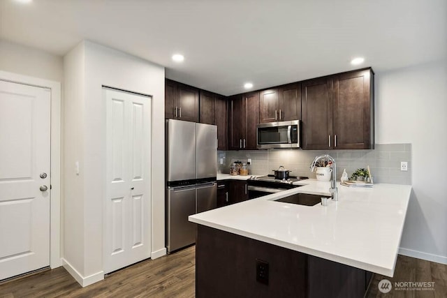 kitchen featuring a sink, stainless steel appliances, dark brown cabinetry, a peninsula, and light countertops