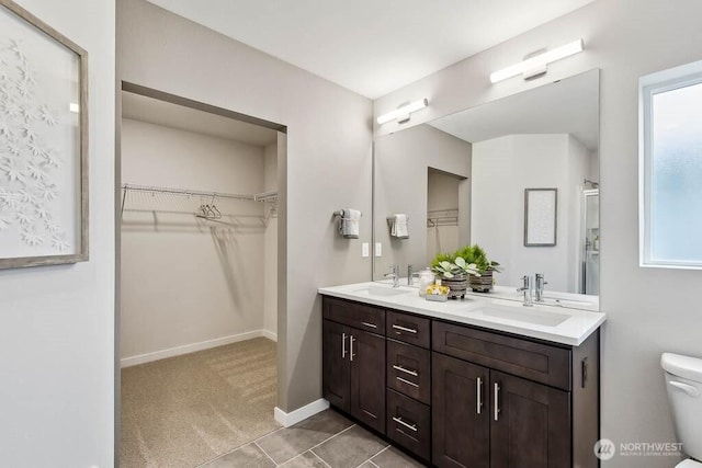 bathroom with double vanity, toilet, baseboards, and a sink