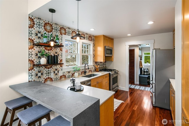 kitchen with a sink, decorative light fixtures, appliances with stainless steel finishes, a peninsula, and dark wood-style flooring