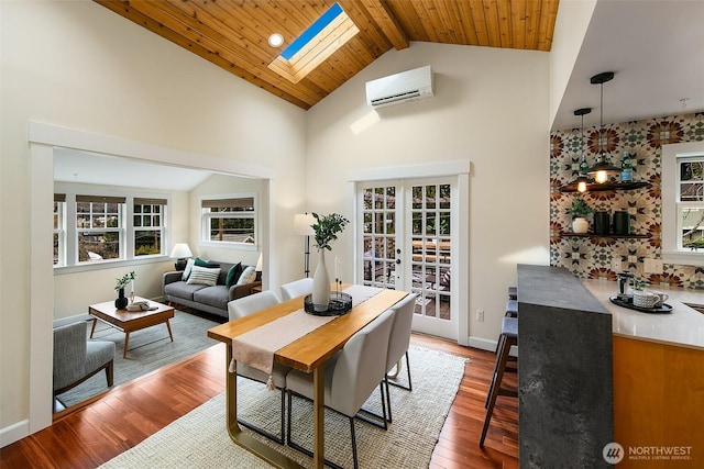 interior space featuring baseboards, an AC wall unit, french doors, a skylight, and wood finished floors