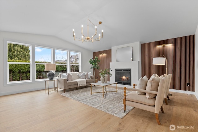 living room with a glass covered fireplace, light wood-style floors, an inviting chandelier, baseboards, and vaulted ceiling