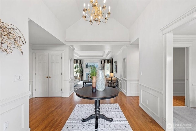 foyer with lofted ceiling, a decorative wall, arched walkways, and light wood-type flooring